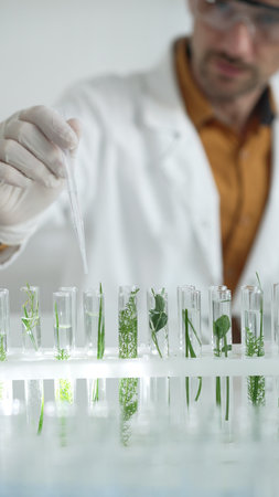 Man scientist wearing a lab coat, white gloves and protective glasses, is dripping liquid from a...