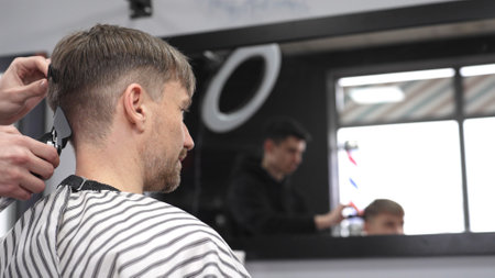 Professional barber trimming male clients hair using electric razor, creating precise haircut in barbershop setting with sleek styling toolsの写真素材