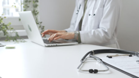 Stethoscope over a medical records are lying on the desk opposite the doctor is typing on a laptop with a in a medical office, suggesting online healthcare or telemedicine services. Medicine conceptの写真素材