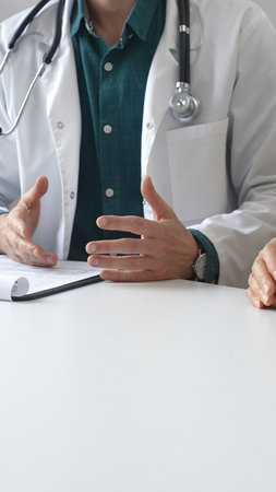 Doctor man wearing medical coat over green shirt, and stethoscope is gesturing with hands while...