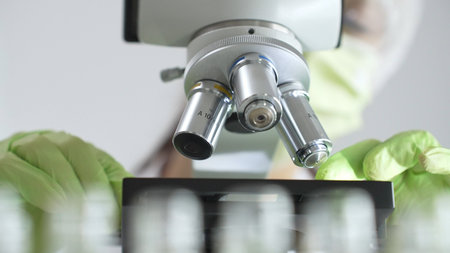 Close up of green gloved hands of a scientist adjusting a microscope in a laboratory, emphasizing...