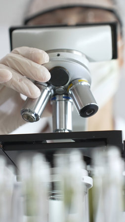 Close up of white gloved hand of a scientist adjusting a microscope in a laboratory. Medicine,...