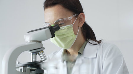 Female professional scientist examining specimen, placing slide under microscope while wearing green...