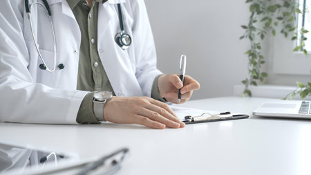 Professional female doctor wearing white lab coat and stethoscope documenting patient information on...
