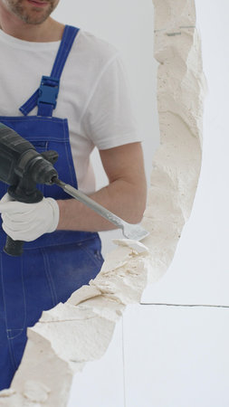 Unrecognizable male construction worker wearing blue overalls and protective white gloves, is...