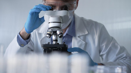 Male scientist researcher wearing blue gloves, protective glasses and medical mask, is using...