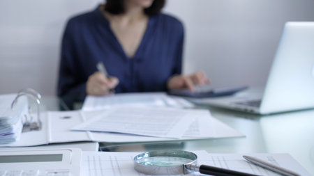 Magnifying glass, white calculator, pen and documents are lying on accountants desk. Businesswoman...