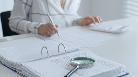 Magnifying glass on financial documents, with an accountant using a calculator and taking notes, emphasizing accounting, finance, and tax preparation. Audit and taxes conceptの写真素材
