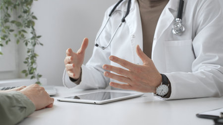 Doctor gesturing with hands while explaining diagnosis to patient using digital tablet during medical consultation in bright modern office. Medicine and health care conceptの写真素材