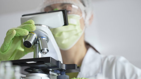 Gloved scientist adjusting a microscope, conducting research in a laboratory setting, surrounded by...