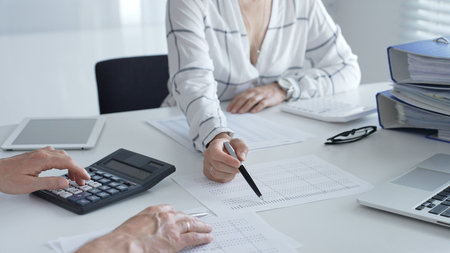 Professional accountants collaborating, reviewing financial reports using calculator, laptop,...