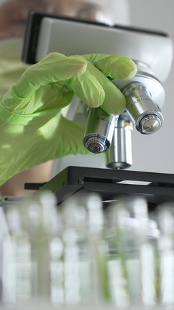 Close up of green gloved hands of a scientist adjusting a microscope in a laboratory, emphasizing...