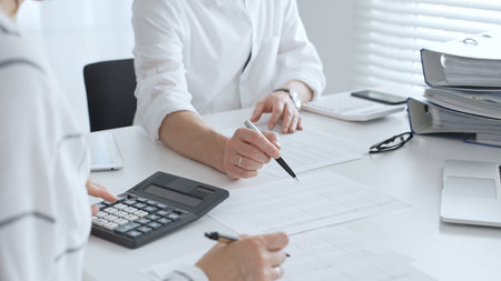 Two accountants collaborating in a well lit office, analyzing financial data and preparing reports...