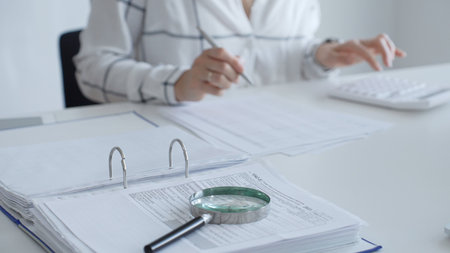 Close up of a magnifying glass on financial documents, with an accountant using a calculator and...