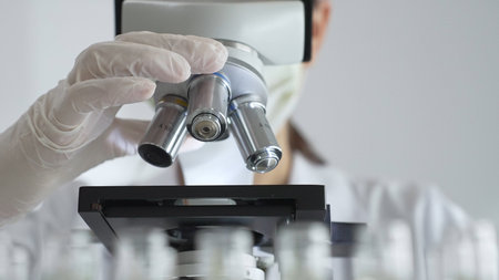 Scientist wearing white gloves adjusting microscope in laboratory setting, conducting scientific...