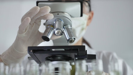Scientist wearing white gloves adjusting microscope in laboratory setting, conducting scientific...