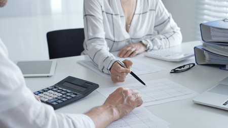 Professional accountants collaborating, reviewing financial reports using calculator, laptop,...