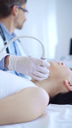 Doctor man wearing white protective gloves is using ultrasound machine to examine neck of female...