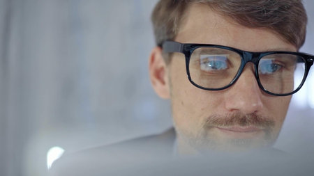 Businessman with glasses looking intently obscured partially by a translucent surface of laptop....