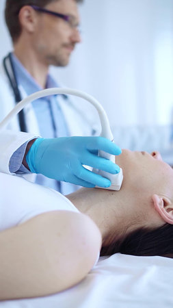 Doctor man wearing blue protective gloves is using ultrasound machine to examine neck of female...