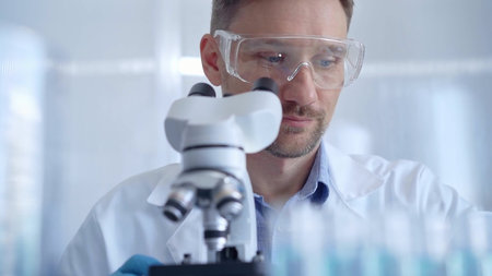 Man scientist with protective glasses and gloves is using microscope in laboratory, portrait of...