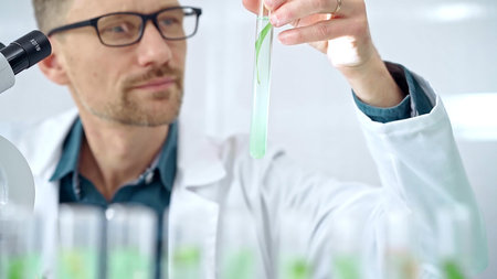 Scientist examining lab tube with a green fluid. Microbiology and science concept