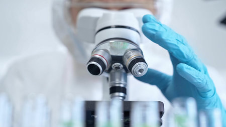 Professional scientist in protective gear is using microscope in a laboratory setting, close-up....