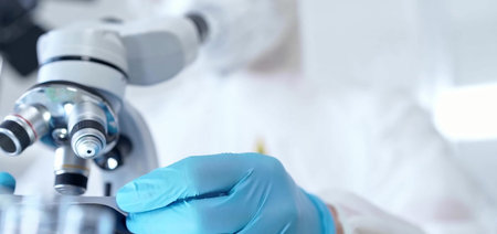Professional scientist in protective gear is using microscope in a laboratory setting, close-up....