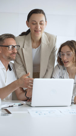 Business people working together, reviewing data on laptop screen, sharing insights during...