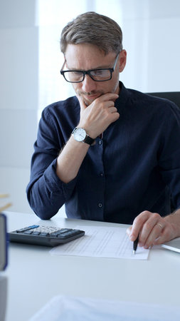 Businessman using a calculator and analyzing financial documents while preparing paperwork at an...