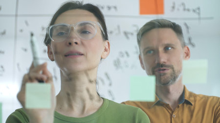 Professional businesswoman gesturing with marker, discussing strategic plans near glass board...