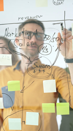 Business people colleagues planning strategy, writing notes on glass wall, collaborating with...