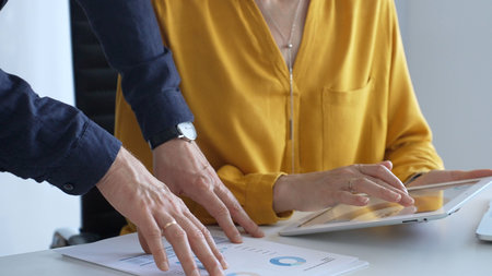 Business colleagues are analyzing data on a digital tablet and printed documents, working together...