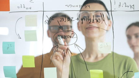 Professional team brainstorming, sharing strategy on glass whiteboard with colorful sticky notes,...
