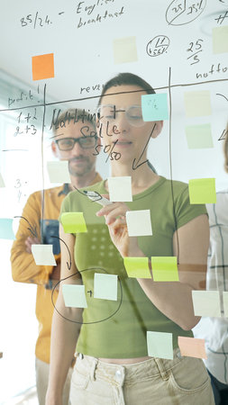 Adult casual dressed businesswoman wearing glasses writing on glass board, marking strategic plan...