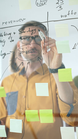 Business people colleagues brainstorming, writing strategy notes on glass board, collaborating with...