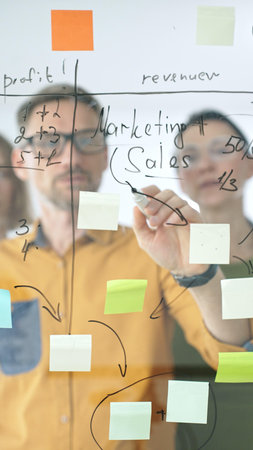 Professional team strategizing, writing collaborative notes on glass board, mapping innovative project workflow with markerの写真素材