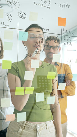 Adult casual dressed businesswoman wearing glasses writing on glass board, marking strategic plan...