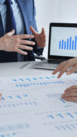 Business people collaborating at a table, discussing financial data and reports with a calculator and laptop displaying charts, focusing on strategy and planning, close up vertical viewの写真素材