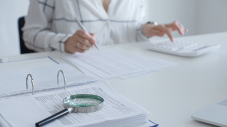Magnifying glass on financial documents, with an accountant using a calculator and taking notes, emphasizing accounting, finance, and tax preparation. Audit and taxes conceptの写真素材