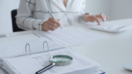Magnifying glass on financial documents, with an accountant using a calculator and taking notes, emphasizing accounting, finance, and tax preparation. Audit and taxes conceptの写真素材