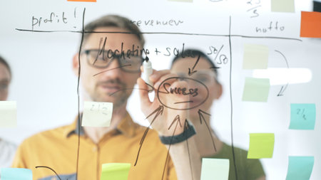 Professional team strategizing, writing collaborative notes on glass board, mapping innovative...