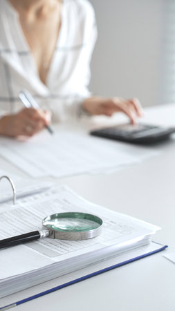 Magnifying glass on financial documents, with an accountant using a calculator and taking notes, emphasizing accounting, finance, and tax preparation, close up vertical view. Audit and taxesの写真素材