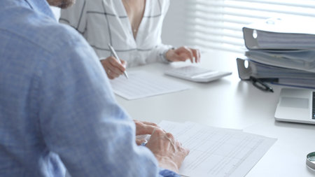 Accounting team working together, reviewing financial reports, using calculator, analyzing data while working at sleek corporate workspace. Audit and taxes conceptの写真素材