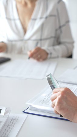 Groupe of professional accountants working together, using a magnifying glass and a calculators, to audit financial reports in their brightly lit office. Audit and taxes conceptの写真素材