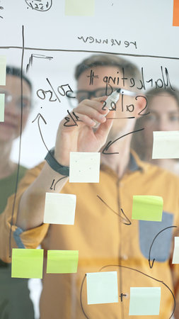 Professional team strategizing, writing collaborative notes on glass board, mapping innovative project workflow with markerの写真素材