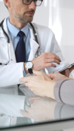 Male doctor consulting female patient, discussing diagnosis and medical history with digital tablet in clinic. Medicine and health careの写真素材