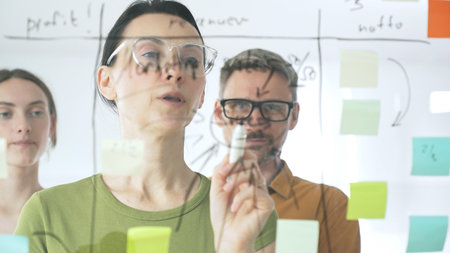 Professional team strategizing, writing collaborative notes on glass board, mapping innovative...