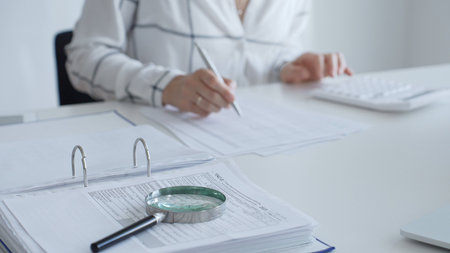 Close up of a magnifying glass on financial documents, with an accountant using a calculator and...