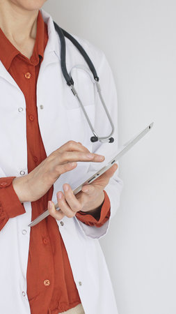 Close up of professional woman doctor, wearing white coat over a brick-red blouse and a stethoscope,...